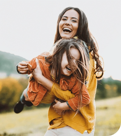 Fotografía de una mujer cargando a una niña, ambas sonríen.