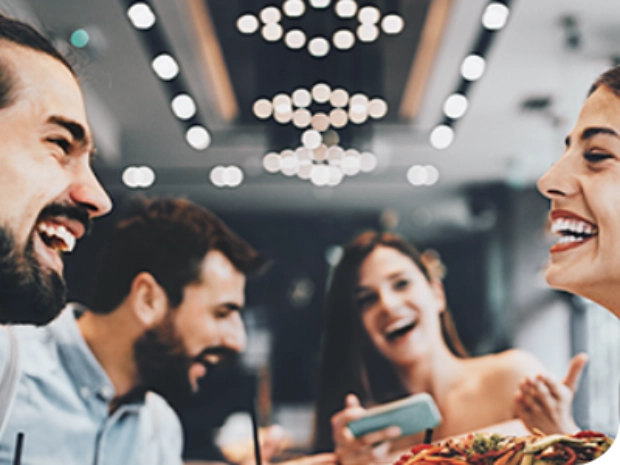 Fotografía de dos mujeres y dos hombres sonrientes, compartiendo una comida en una mesa.