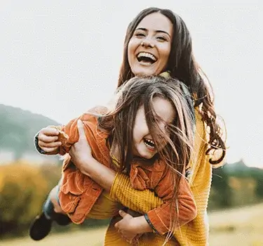 Fotografía de una mujer cargando a una niña, ambas sonríen.