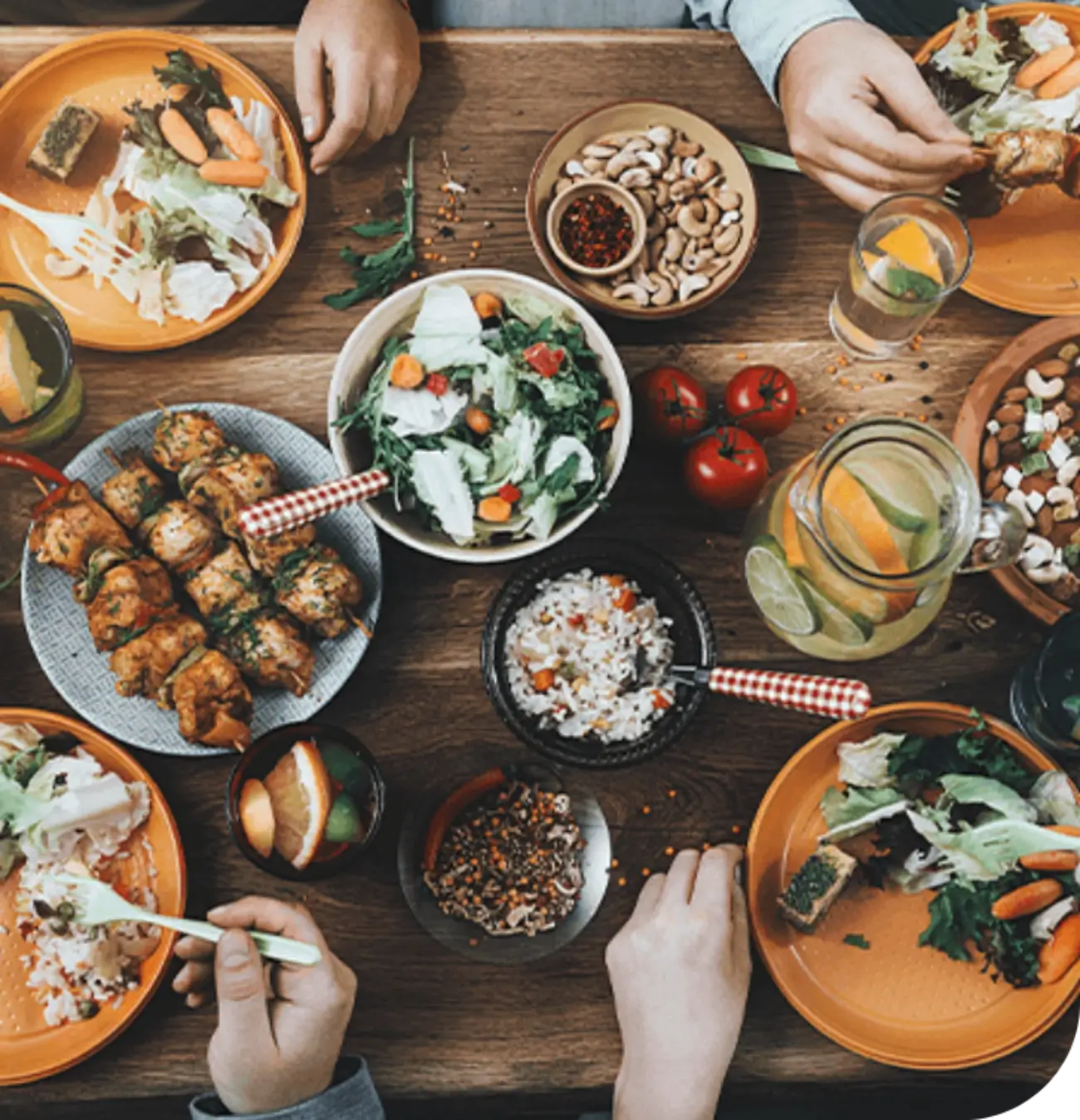 Fotografía de una mesa con diferentes platillos, condimentos y bebidas. Se ven los brazos de cuatro personas comiendo.